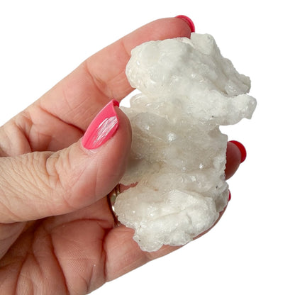 Hand holding a white cave calcite (aragonite) crystal formation against a white background