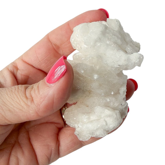 Hand holding a white cave calcite (aragonite) crystal formation against a white background