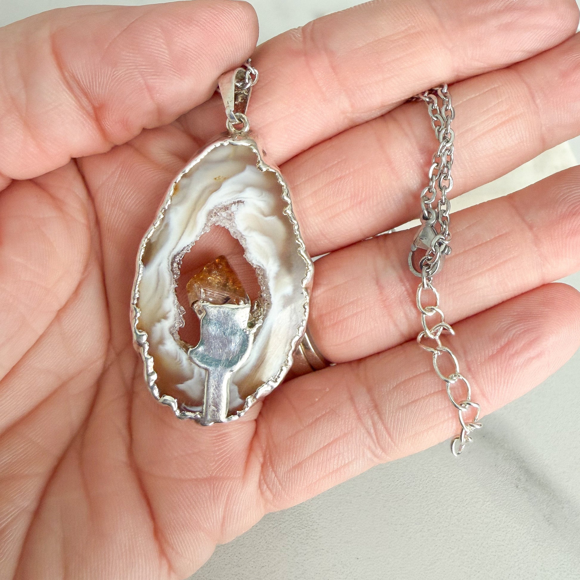 Close-up of silver plated agate geode slice pendant with raw citrine crystal held in hand
