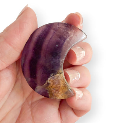 Hand holding Banded purple fluorite moon carving with rich purple stripes, white quartz areas, and earthy natural inclusions.