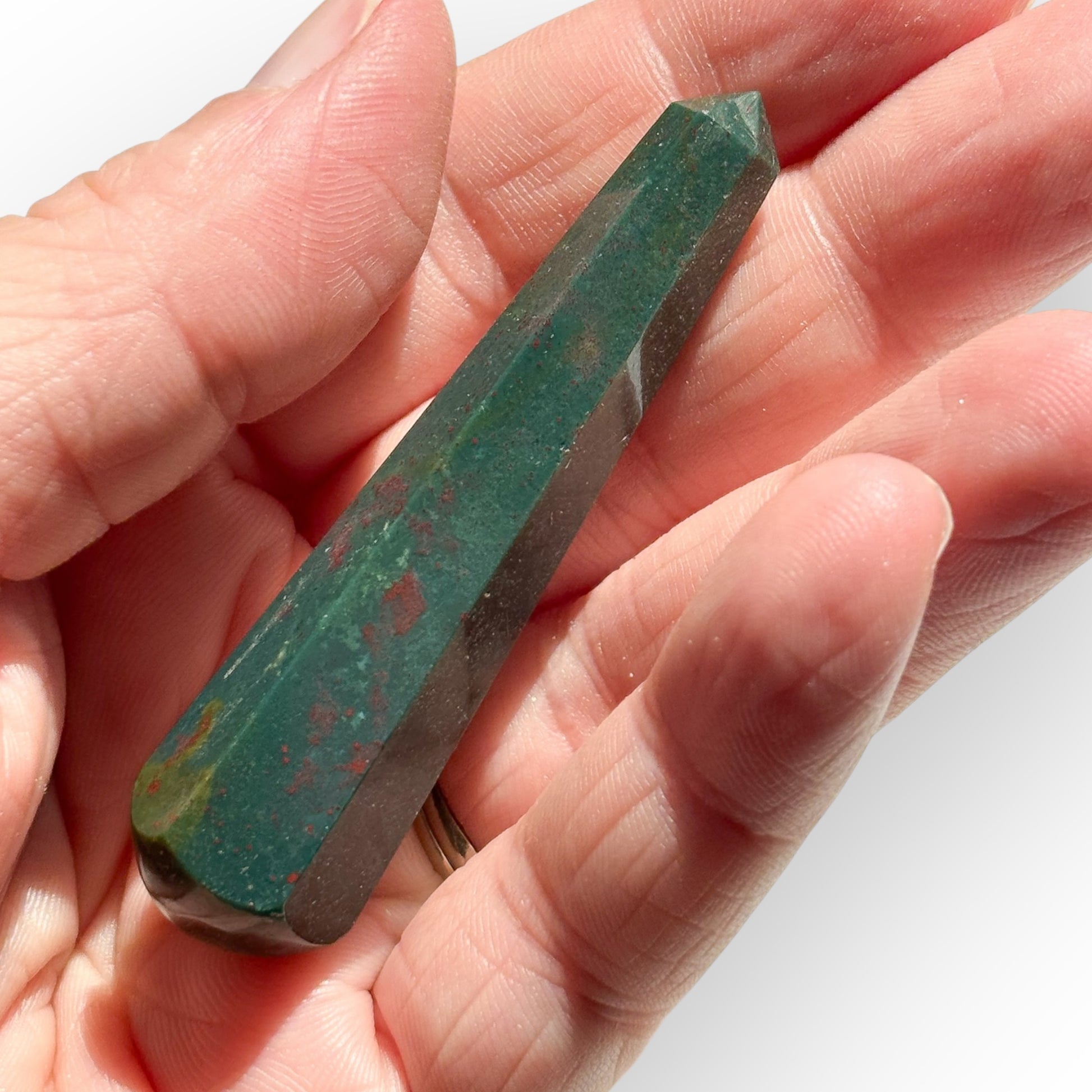 Bloodstone wand held in hand, showing natural red spots and deep green hues in sunlight.