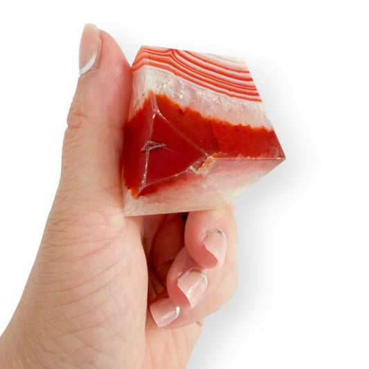 Handheld Carnelian Agate display cube with layered red agate bands and translucent quartz-rich areas.