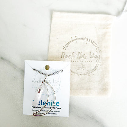 Silver plated crescent moon with selenite pendant necklace displayed on Rock This Way Crystal Shop packaging with included polishing cloth.