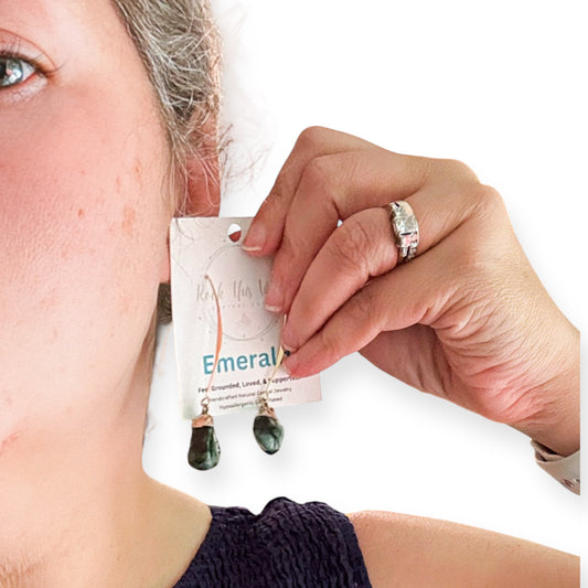 Woman holding raw emerald earrings near ear to show size and fit.