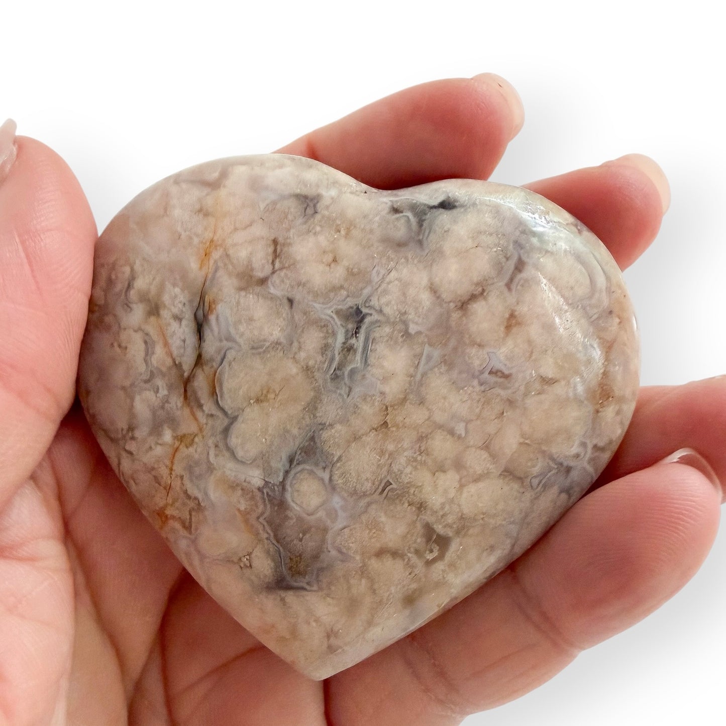 Hand holding a Flower Agate heart with clustered blossom formations, pale gray banding, and natural crystal-filled cavities.