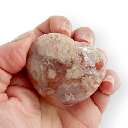 Hand holding a Madagascar Flower Agate heart displaying delicate flower-like inclusions and translucent peach chalcedony.