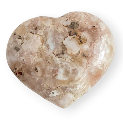 Polished Flower Agate heart featuring soft blush pink and cream blossom formations with natural chalcedony patterns and subtle earthy inclusions.
