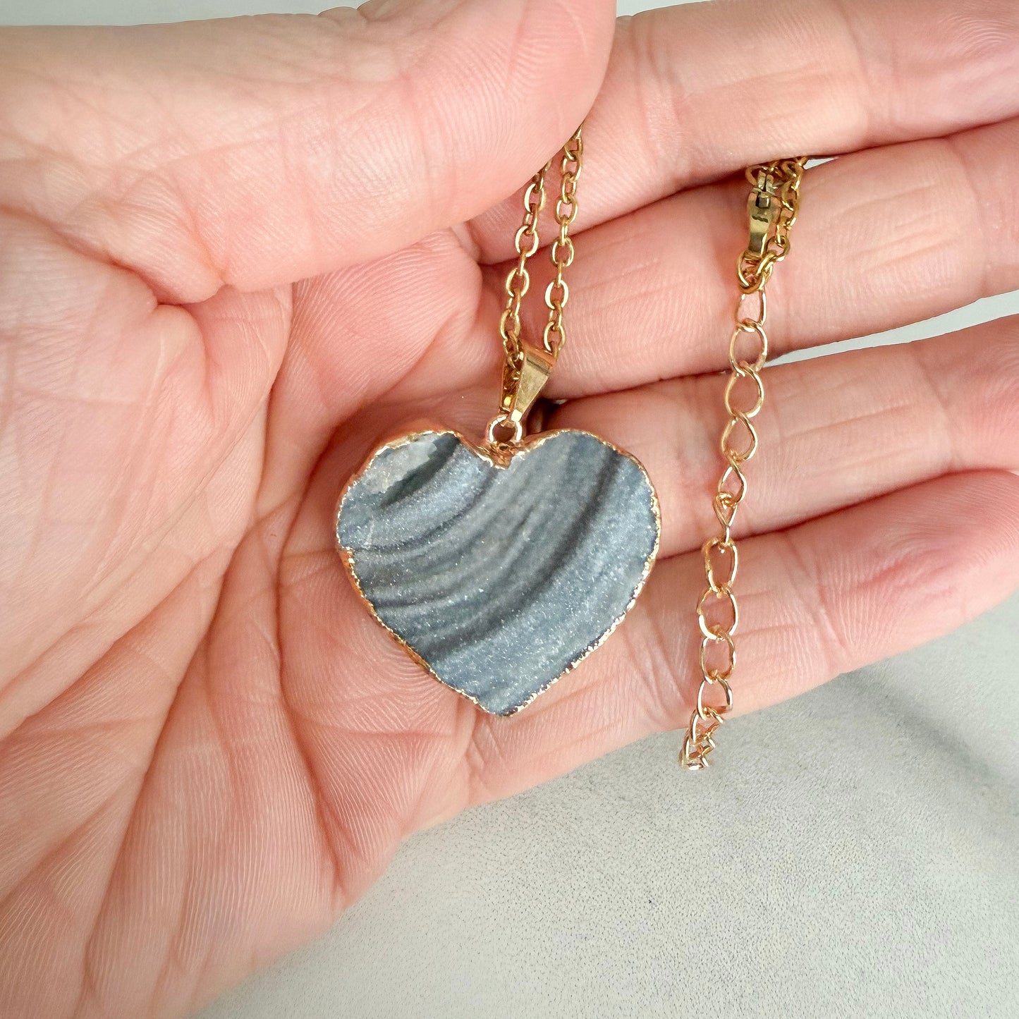 Close up of gold plated heart drusy pendant highlighting natural crystal texture, banding, and soft sparkle.