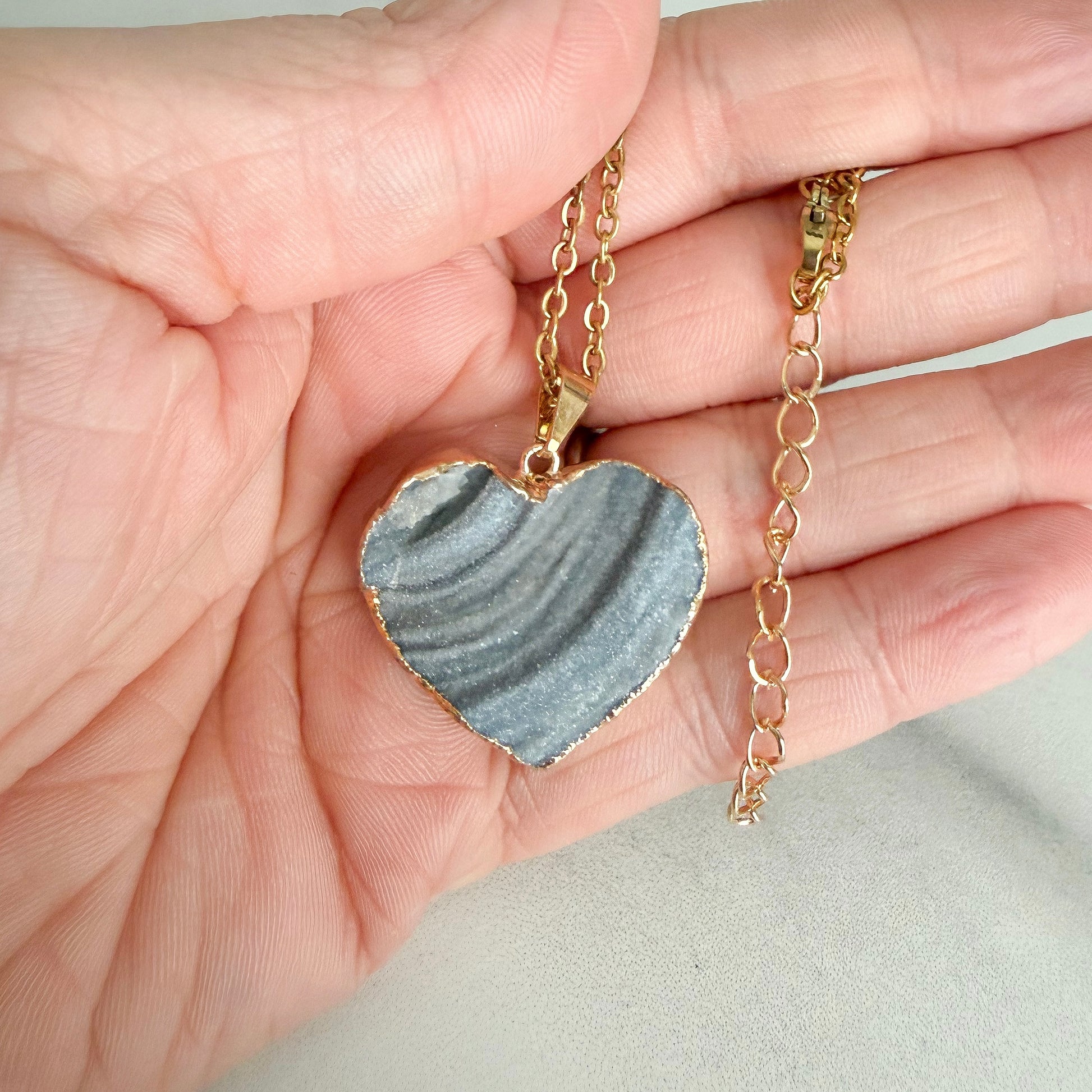 Close up of gold plated heart drusy pendant highlighting natural crystal texture, banding, and soft sparkle.