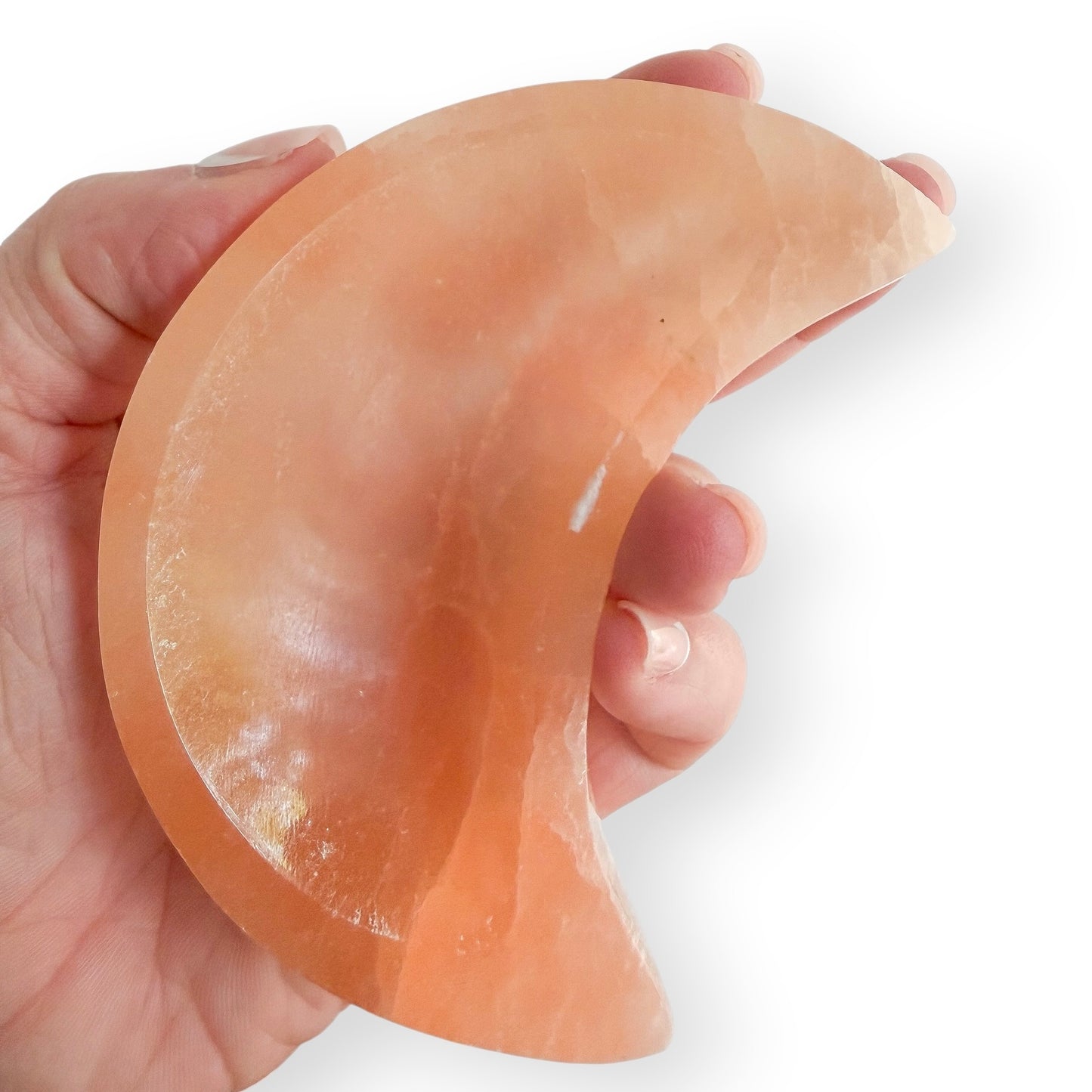 Hand holding Large peach-orange Satin Spar moon-shaped crystal bowl carved from natural Satin Spar with a silky sheen.