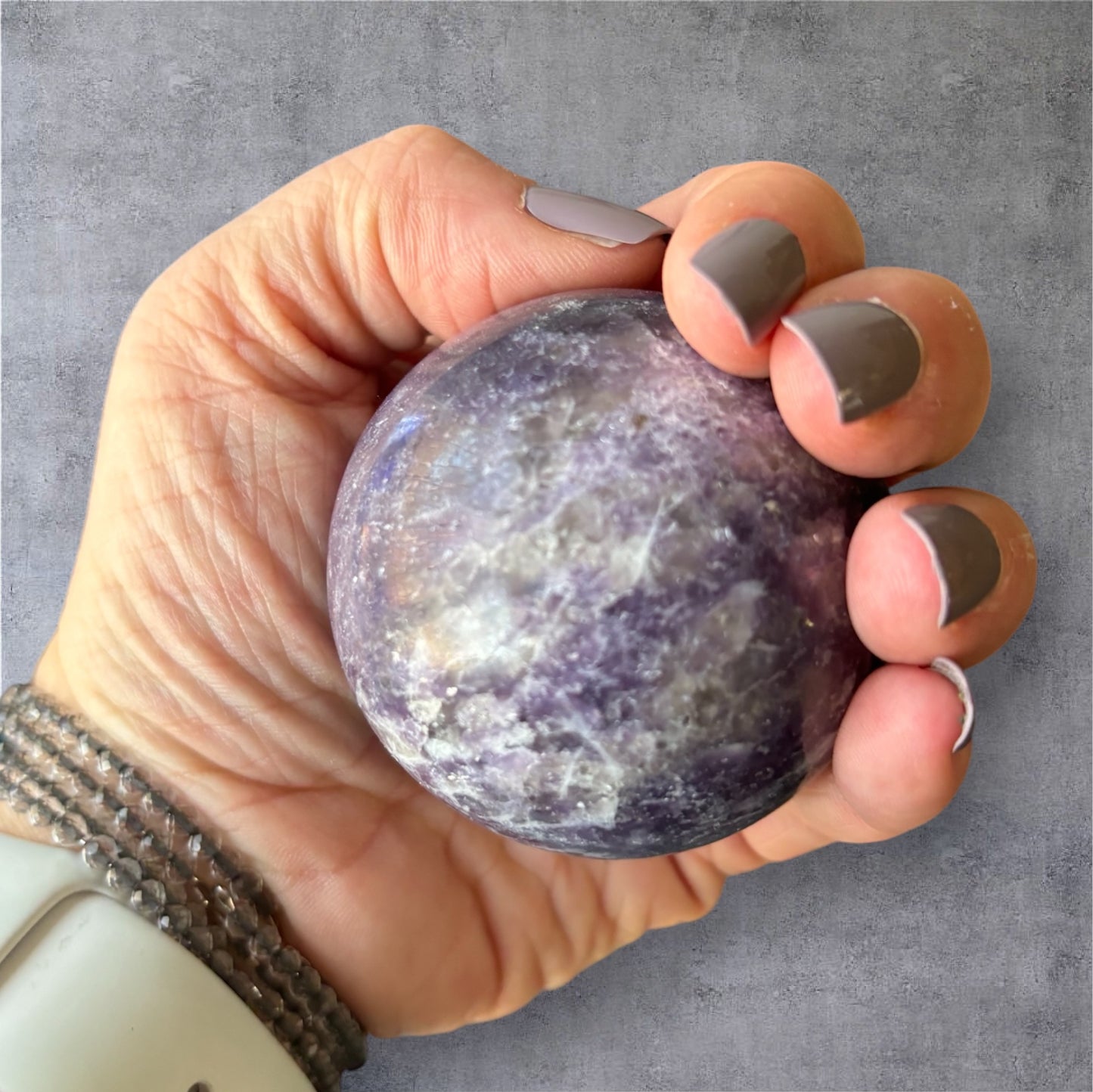 Lepidolite sphere held in hand showing crystal size and texture