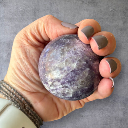 Lepidolite sphere held in hand showing crystal size and texture