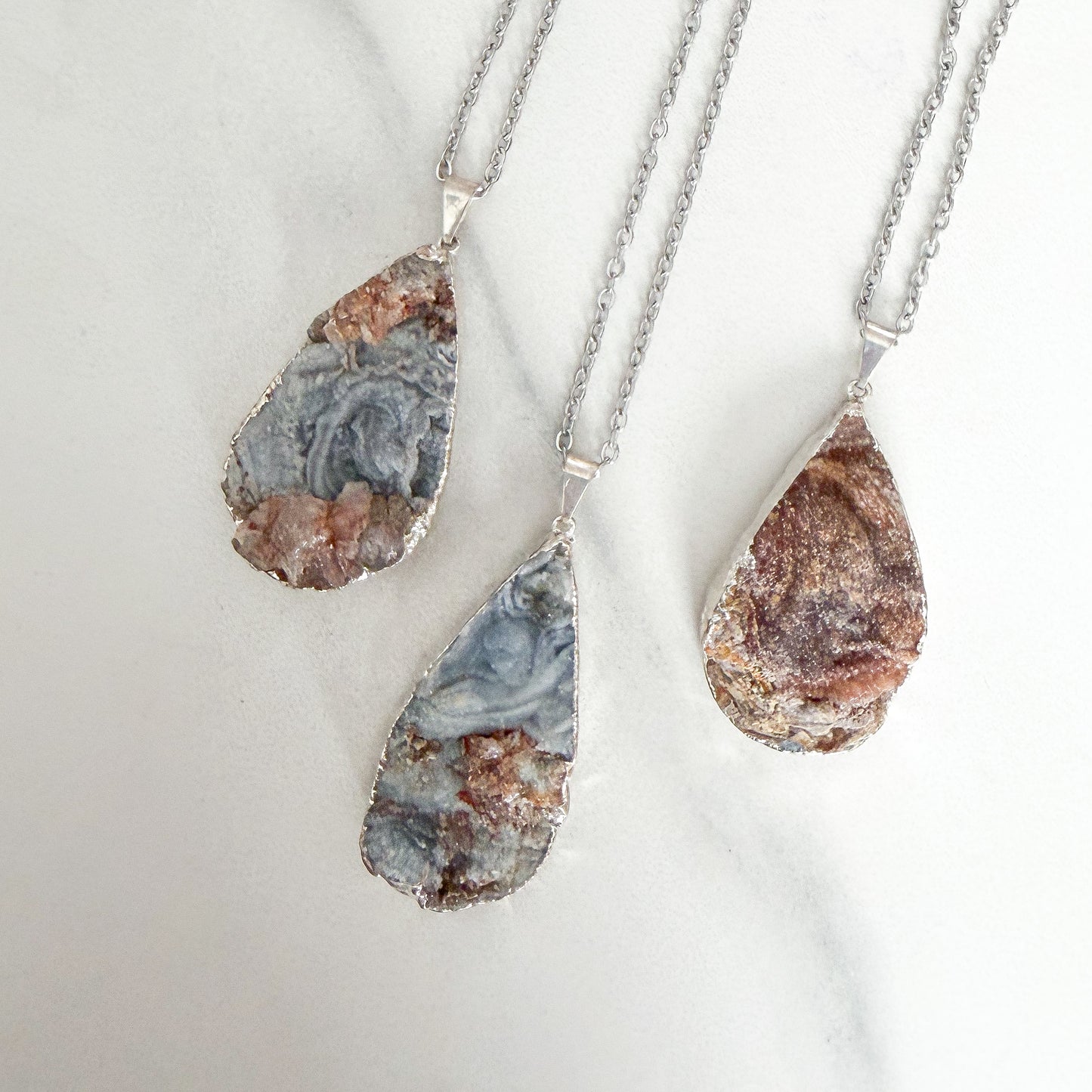 Multi-colored teardrop drusy crystal pendant necklace with sterling silver plating on a stainless steel chain.