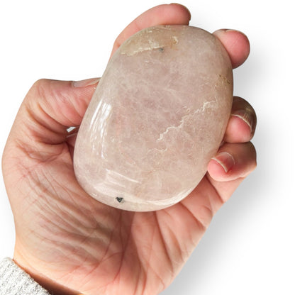 Hand holding a rose quartz crystal against a white background