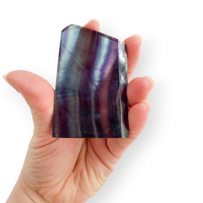 Rainbow Fluorite slab held in hand showing vibrant purple, indigo, teal, and blue natural banding.