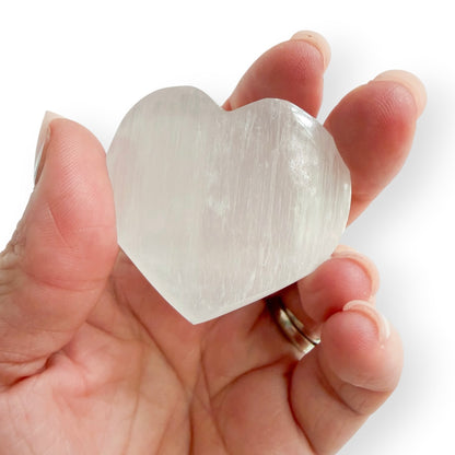 Hand holding a polished Satin Spar heart showing size and luminous white coloring.