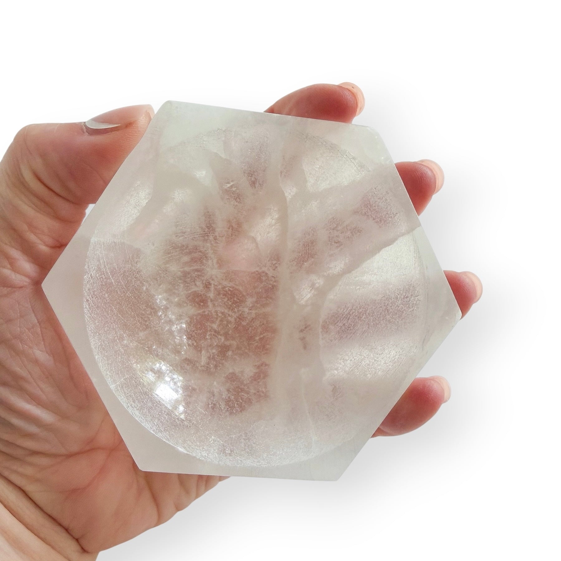 Hand holding Hexagonal Satin Spar crystal bowl featuring a smooth concave center and pearly glow.