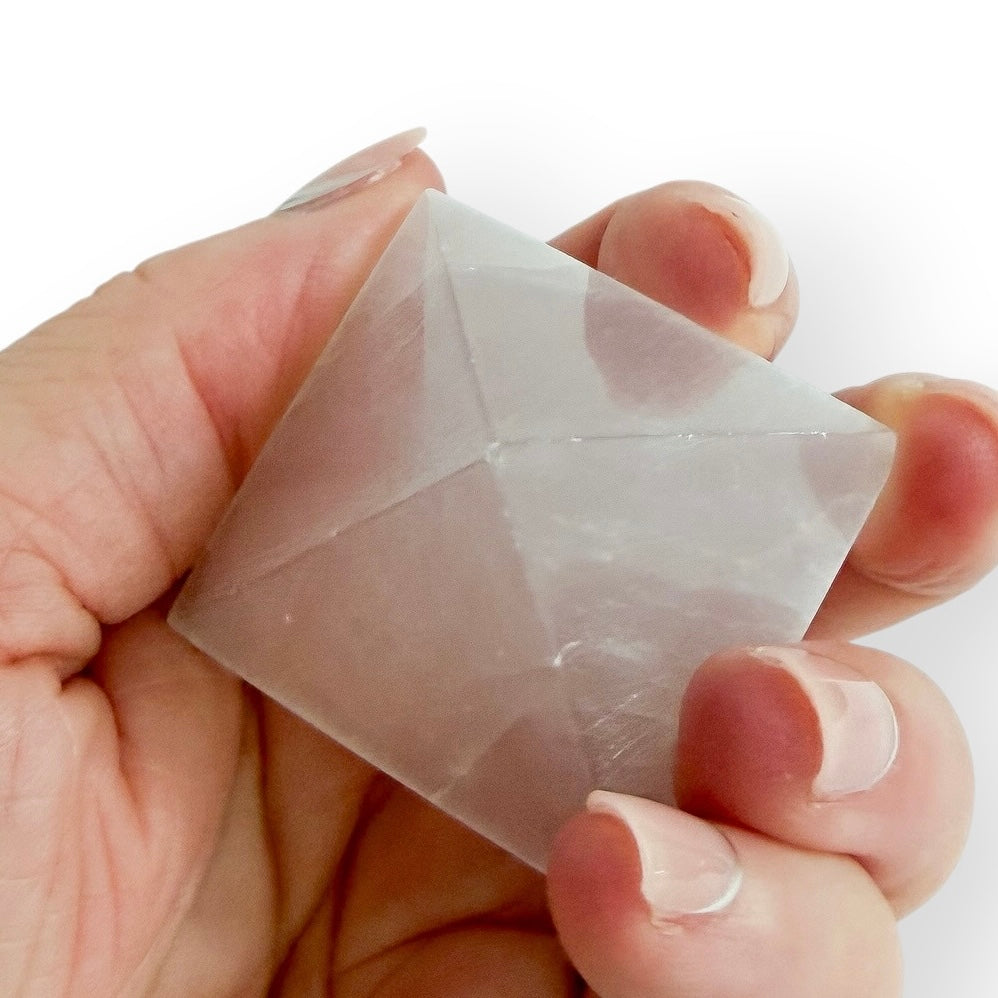 Hand holding Polished Satin Spar pyramid featuring natural fibrous banding and a soft luminous glow.