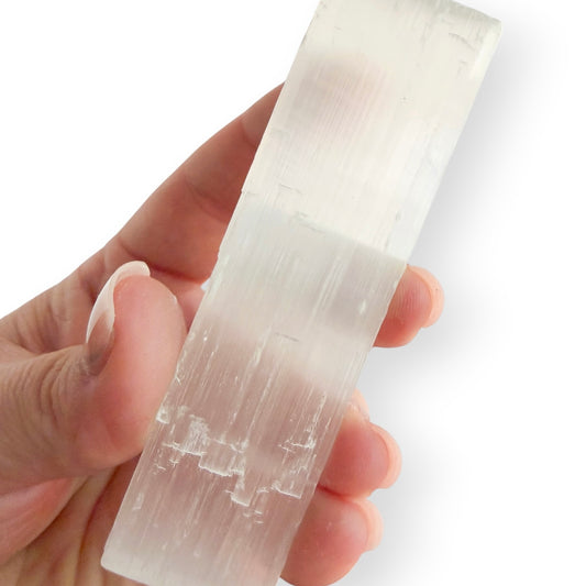 Hand holding a satin spar selenite charging plate showing its size and natural fibrous texture.