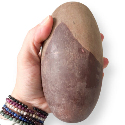 Hand holding Shiva Lingam Stone A to show size and natural texture, with visible surface chips.
