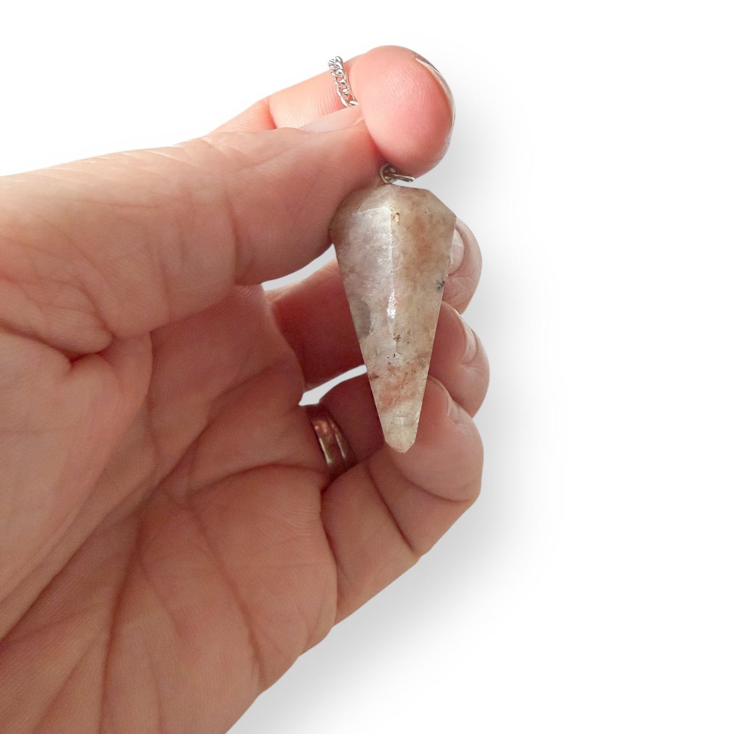 Hand holding a natural Sunstone pendulum showing peach and cream crystal tones on a silver chain
