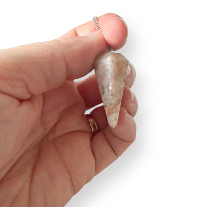 Hand holding a natural Sunstone pendulum showing peach and cream crystal tones on a silver chain